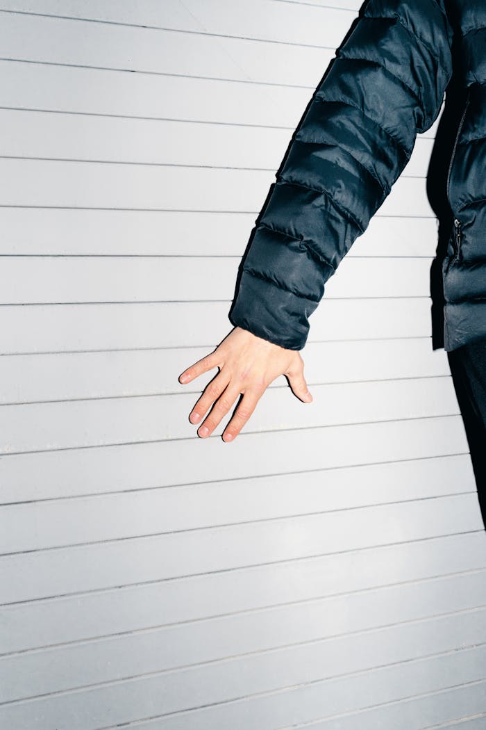 Human hand and black jacket against a white wall with horizontal lines.