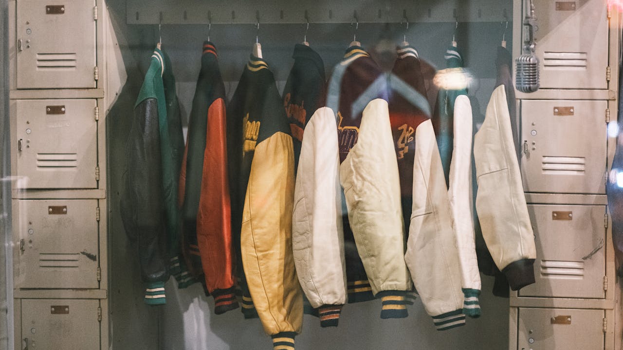 Collection of vintage varsity jackets hanging in a locker room creates a nostalgic vibe.
