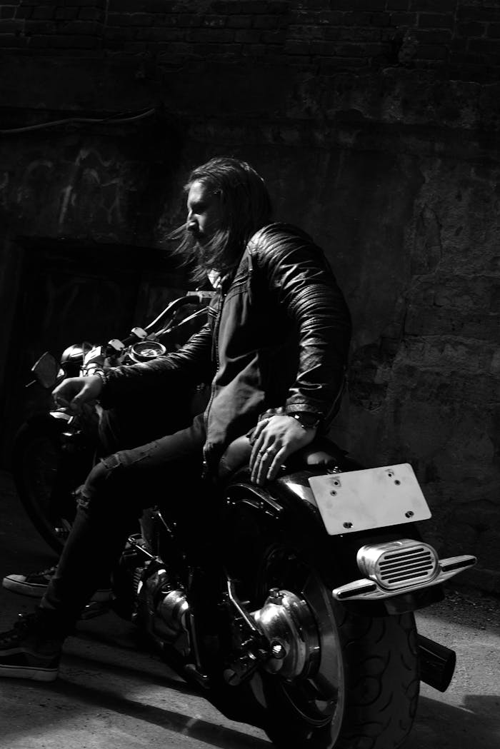Grayscale image of a biker sitting on a motorcycle with a moody backdrop.